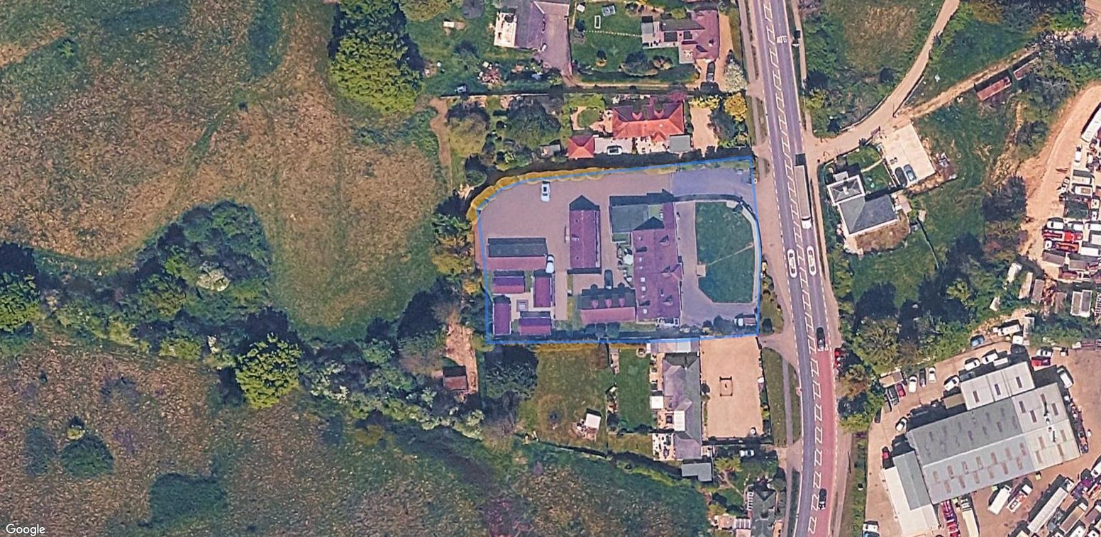 Flimwell__Forest_Edge_Motel - SJD Projects Aerial view of a fenced parcel with red-roof buildings inside a blue boundary, adjacent to a main road and surrounding greenery.