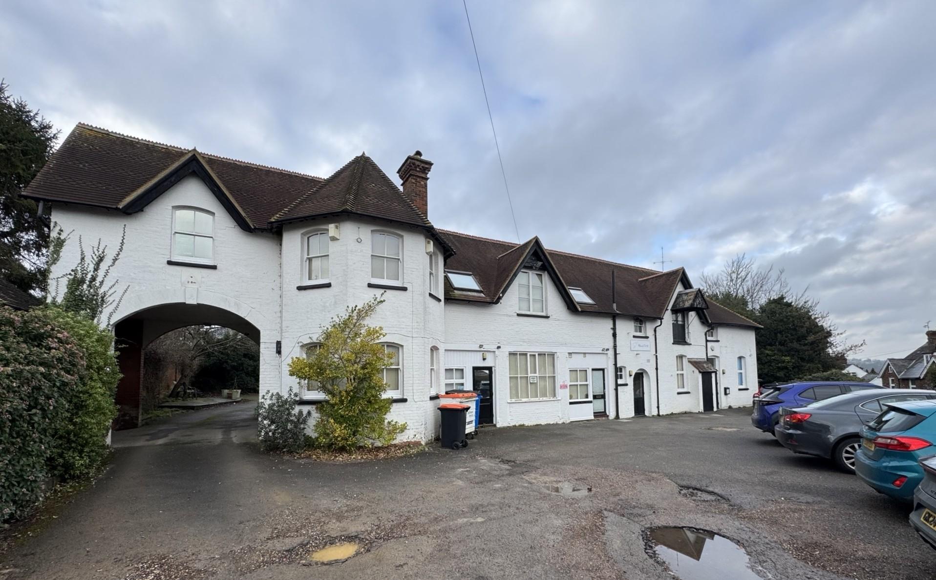 Hawkhurst__Cranbrook_Road - SJD Projects White brick townhouse complex with a large archway on the left, row of attached houses, and cars parked along the street under a cloudy sky.