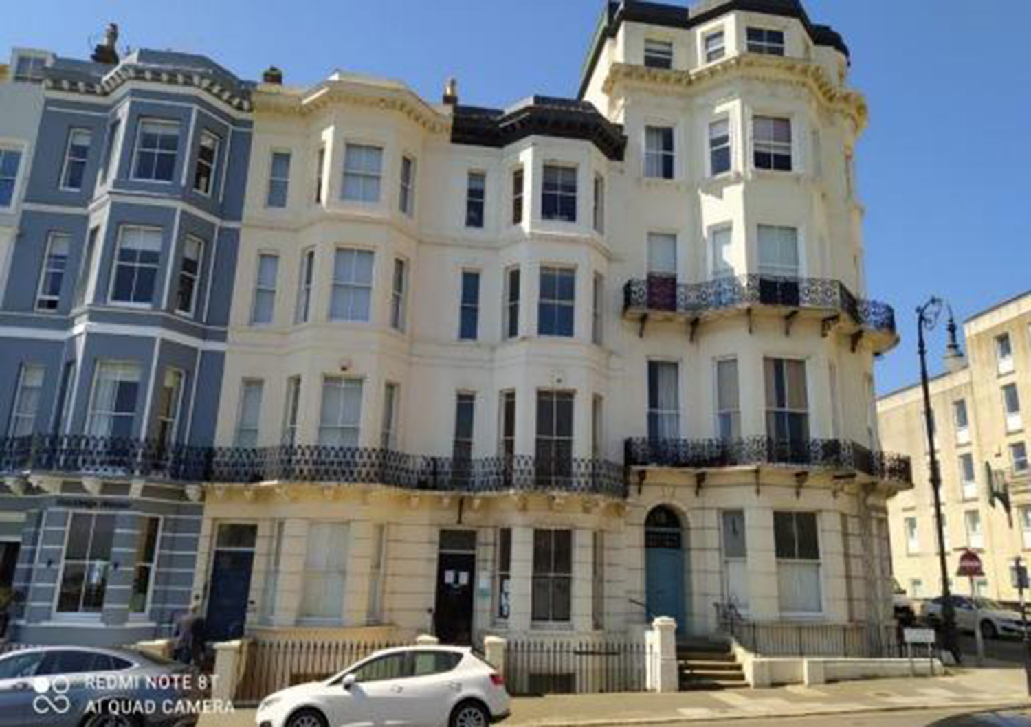 St_Leonards_on_Sea__Warrior_Square - SJD Projects Row of ornate Victorian townhouses with bay windows and iron balconies on a sunny street.